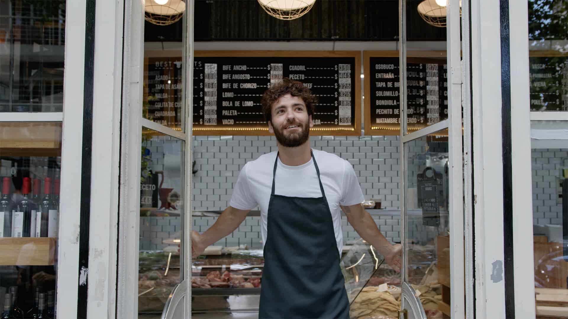 A modern butcher and wine shop owner smiling and opening his shop door, highlighting entrepreneurship and business growth.