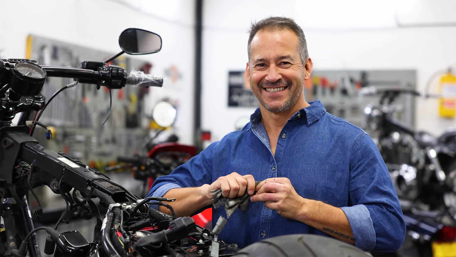 A motorbike shop owner smiling while working on fixing a motorbike, showcasing expertise and business dedication, supported by AFB loans.